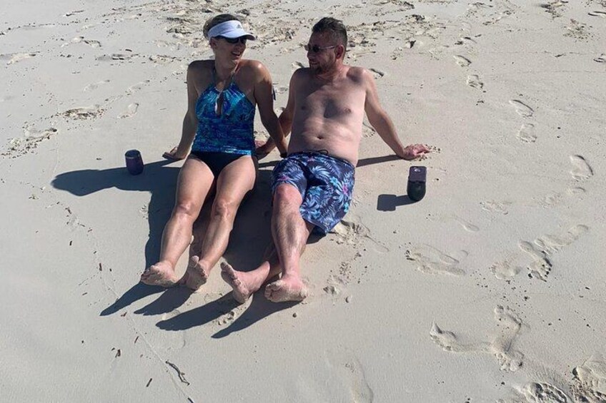 Deux personnes assises sur une plage de sable, avec des empreintes de pas tout autour d’elles. 2