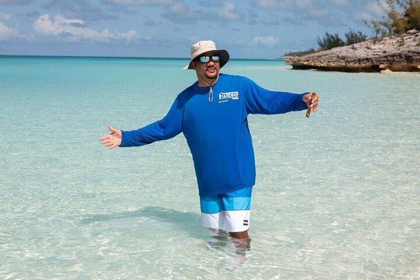 A person standing in shallow water with arms outstretched, wearing a blue long-sleeve shirt and white shorts. 5