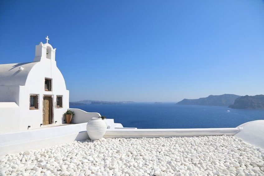 A white building with a cross on top, a large white pot, and a pebble-covered ground. 5