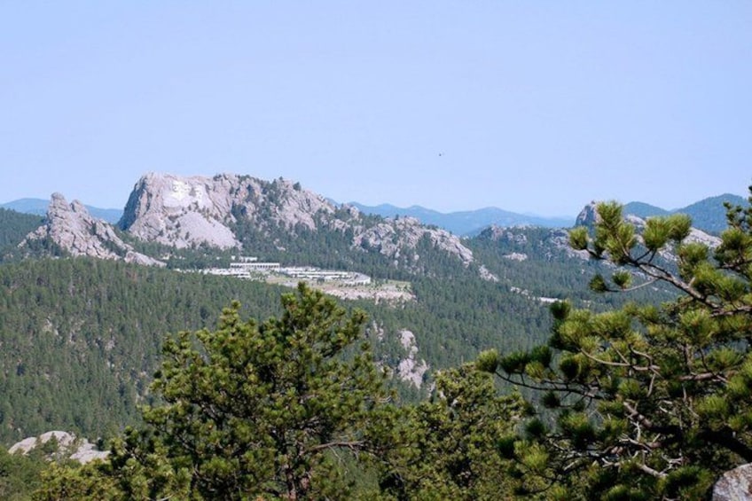 A mountainous landscape with a prominent rocky peak, dense forest, and a building complex in the valley. 3