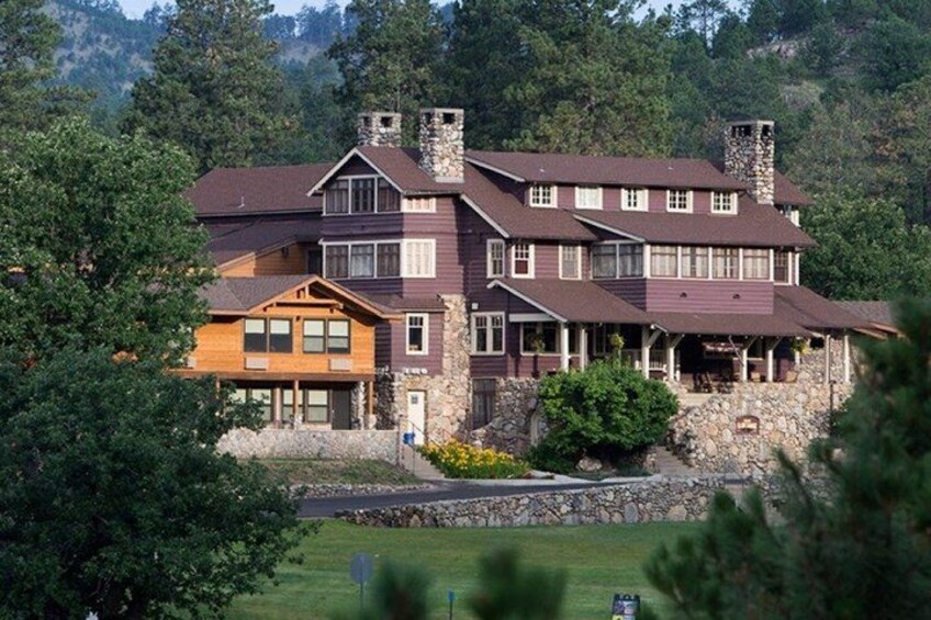 A large, multi-story house with a stone foundation, surrounded by lush greenery and trees. 4