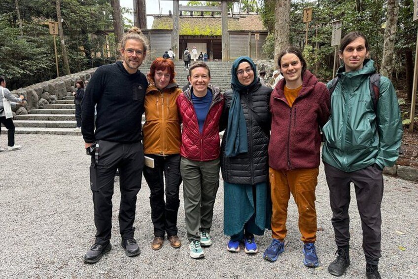 A group of people standing on a gravel path with trees and a building in the background. 3
