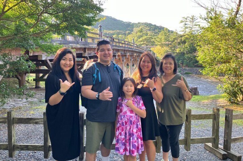 A group of people posing in front of a wooden bridge with a river and hills in the background. 5