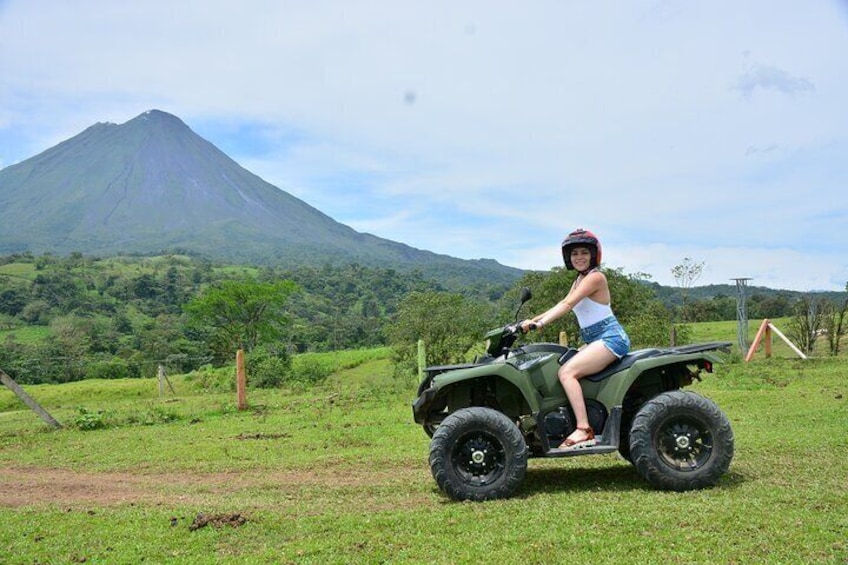 A person riding an ATV in a grassy field with a mountain in the background. 1