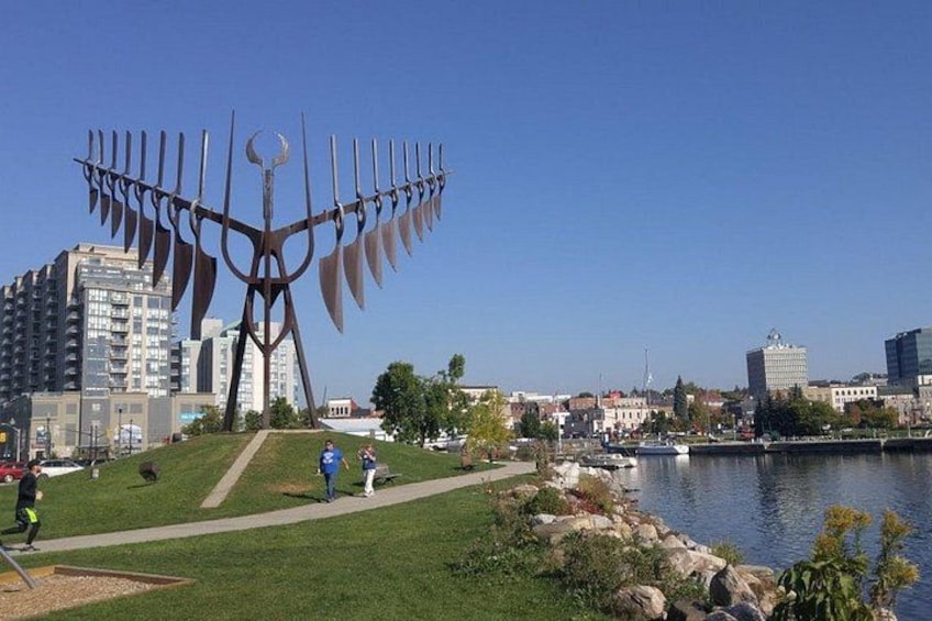 Eine große Metallskulptur in einem Park mit einem Fluss und Gebäuden im Hintergrund. 2