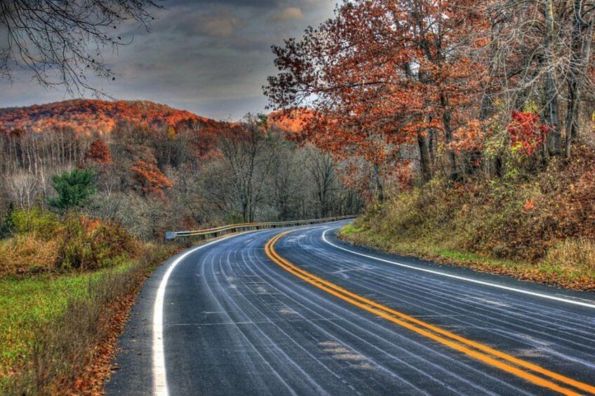 A winding road with yellow centerline, surrounded by autumn foliage and hills. 2