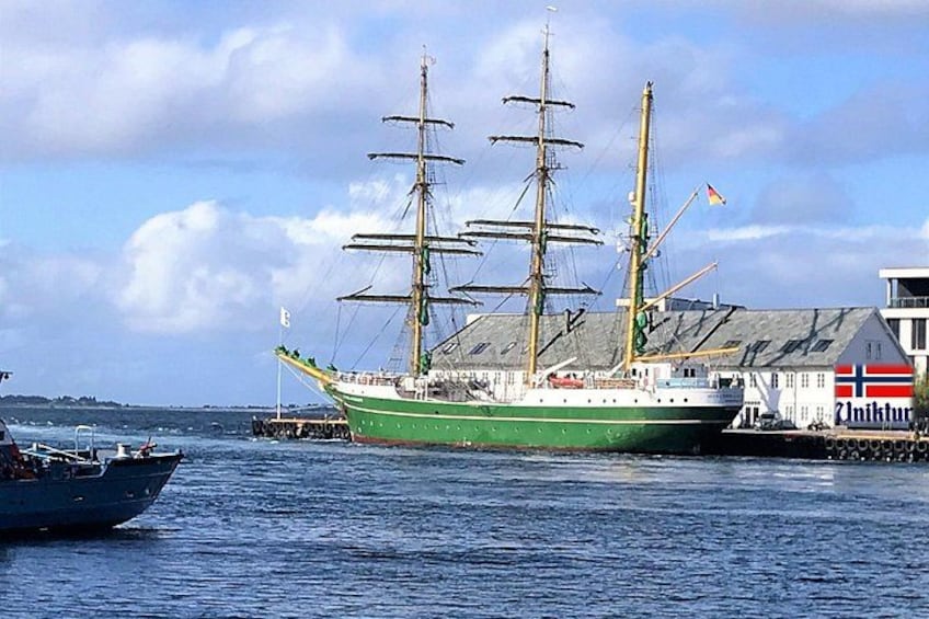 A green ship docked at a harbor with a white building featuring a Norwegian flag. 1
