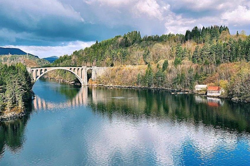 A stone bridge over a calm river, surrounded by forested hills. 4