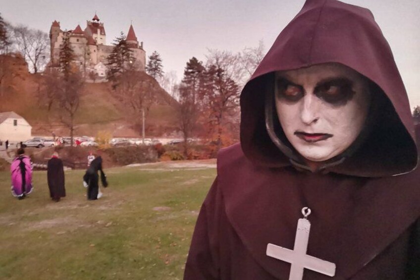 Una persona con una capa oscura y una cruz, un castillo al fondo, y una zona con césped. 2