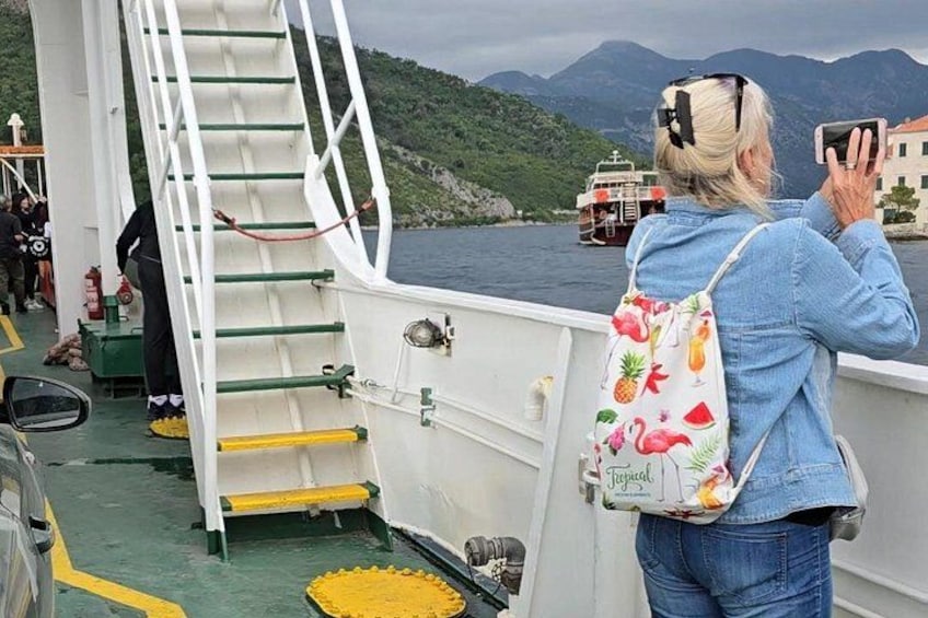 A person taking a photo with a smartphone, a staircase on a boat, and a body of water with mountains in the background. 4