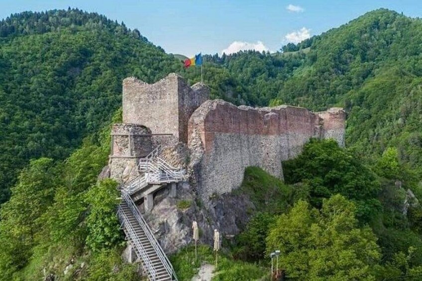 A historical stone fortress with a staircase leading up to it, surrounded by lush green hills. 1