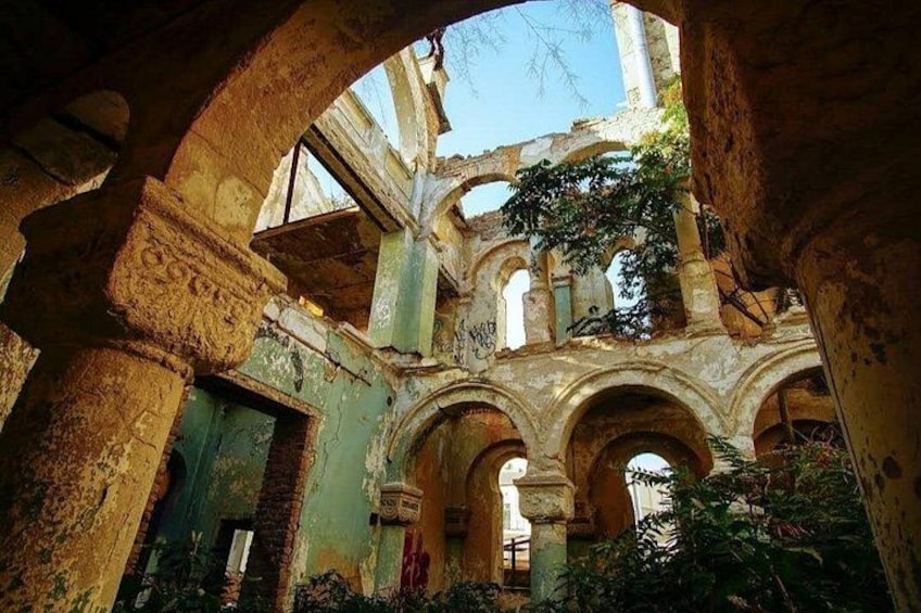 An ancient ruin with arches and columns, overgrown vegetation, and a partially intact structure. 5
