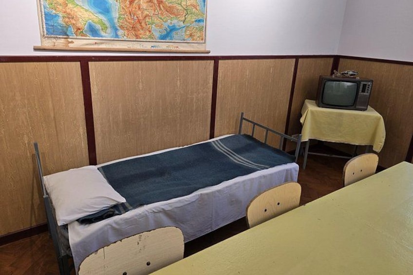 A small room with a single bed, a table, a chair, and a television on a table. 3