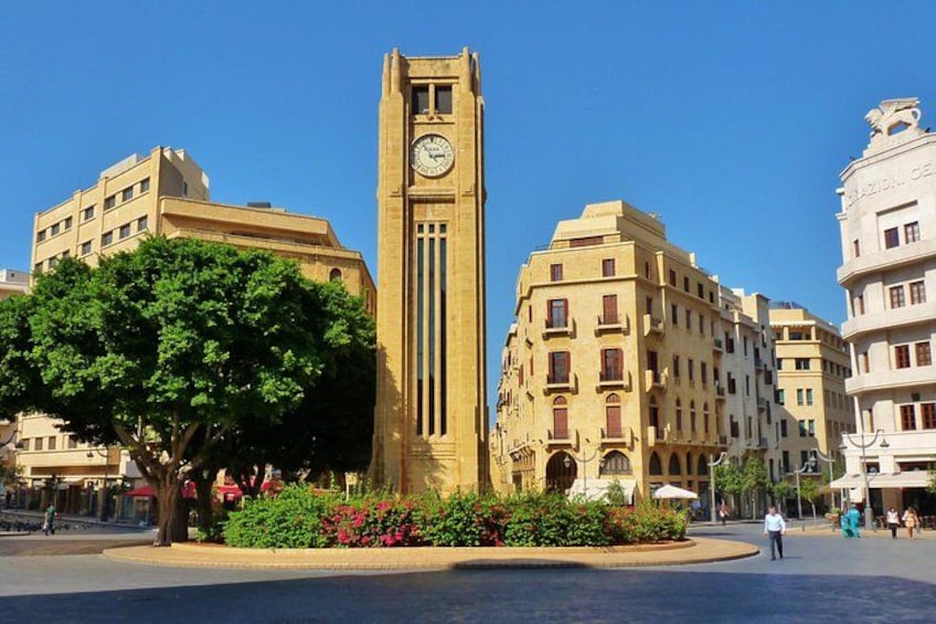 A clock tower, a tree, and buildings in a square. 1