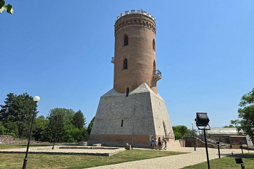 A historic tower with a conical roof, surrounded by a grassy area and trees. 3