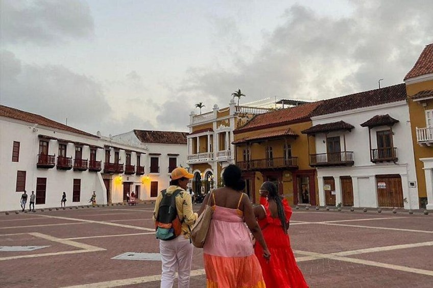 A colonial-style plaza with buildings, a cloudy sky, and people walking. 2