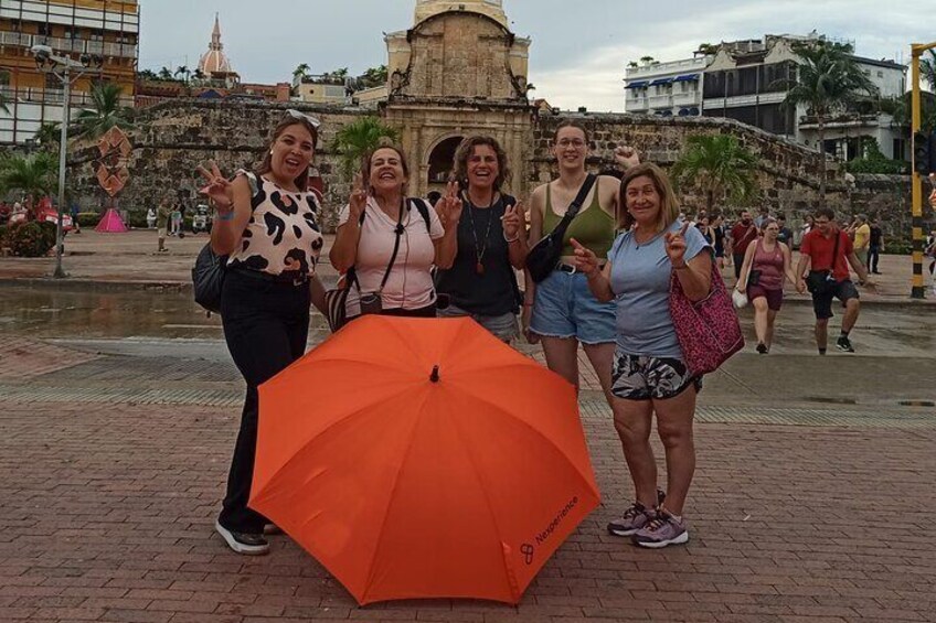 A group of people posing with an orange umbrella in front of a historic building. 5