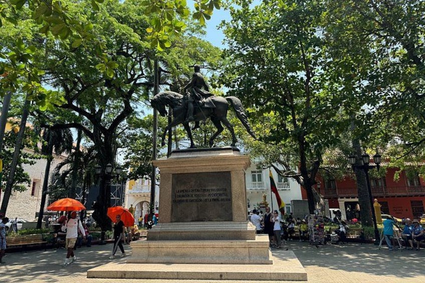 A statue of a man on a horse in a public square with trees and buildings in the background. 4