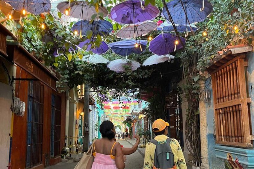 Un estrecho callejón con sombrillas colgantes y vegetación. 1