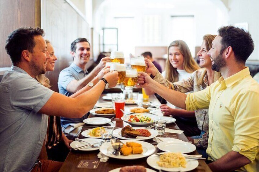 Un grupo de personas brindando con vasos de cerveza en una larga mesa llena de diversos platos. 1