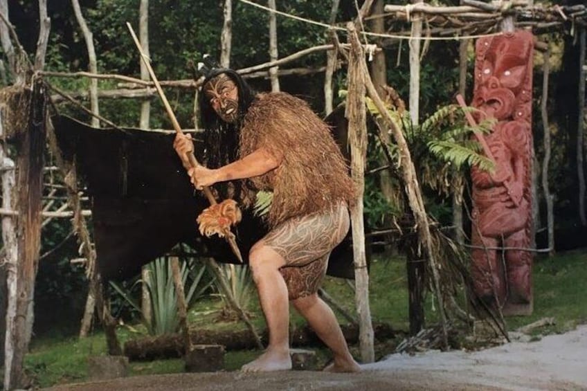 A person in a natural setting with a hut and a totem pole. 3