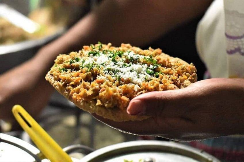 A person holding a flatbread with a topping, possibly a type of stuffed bread or pastry. 1