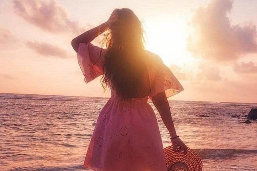 A person in a pink dress standing at the beach with the ocean and a sunset in the background. 2