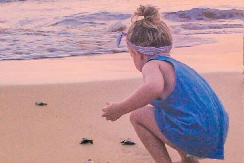 A child in a blue dress playing on a sandy beach with the ocean in the background. 4