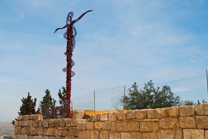 A tall metal sculpture with a snake-like design, a stone wall, and a chain-link fence in the background. 4