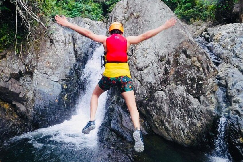 A person jumping off a waterfall in a forested area. 2