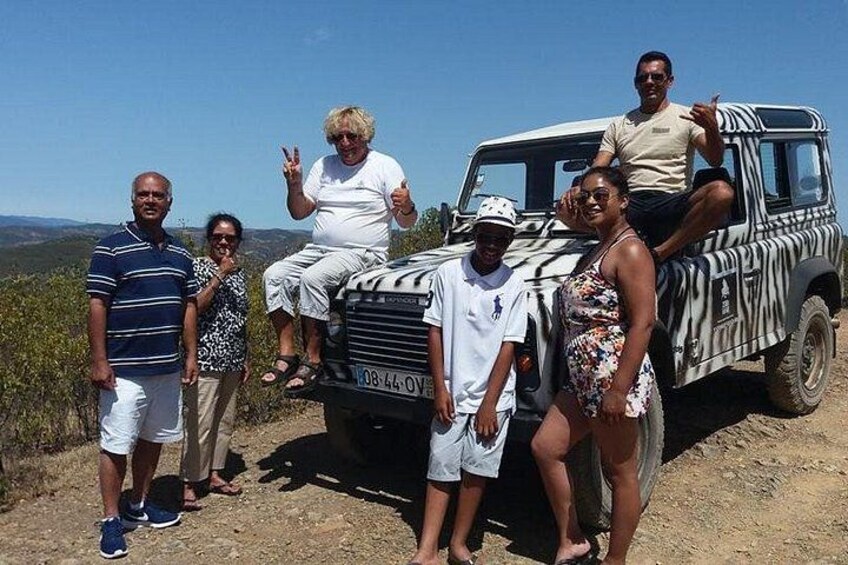 A group of people posing in front of a zebra-striped vehicle on a dirt road with a scenic landscape in the background. 5