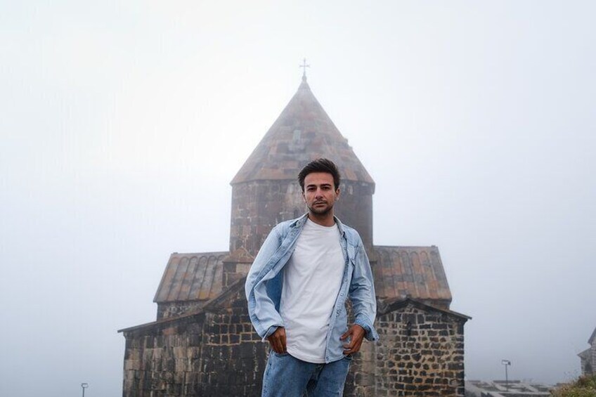 A person standing in front of a stone building with a pointed roof and a cross on top. 3