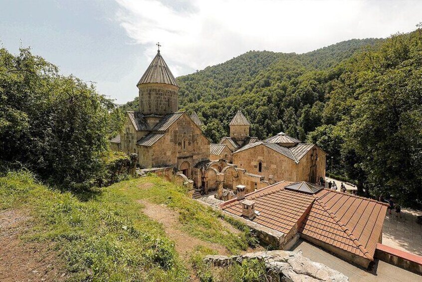 A historic church complex with multiple buildings and a prominent bell tower, surrounded by lush green hills. 1