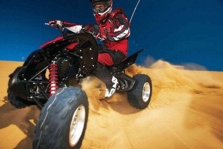 A person riding a quad bike on a sandy surface. 4