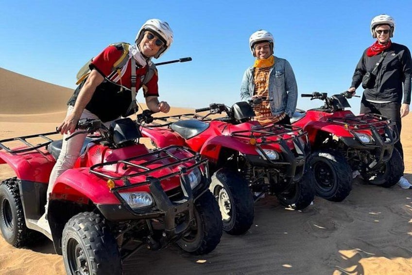 Three people standing next to red ATVs in a desert. 2