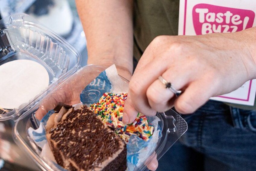 Hands holding a cake with sprinkles and a container of white powder, possibly sugar. 3