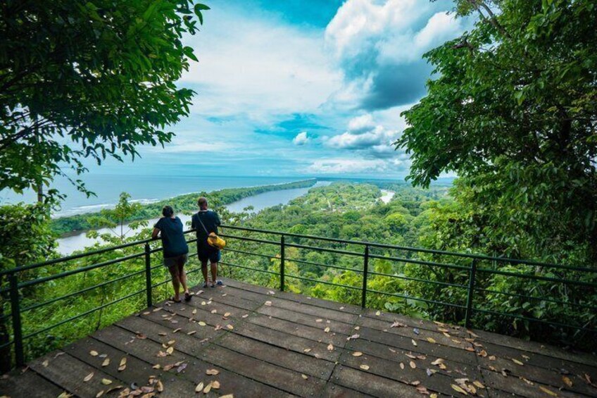 Two people on a wooden viewing platform overlooking a river and forested landscape. 1