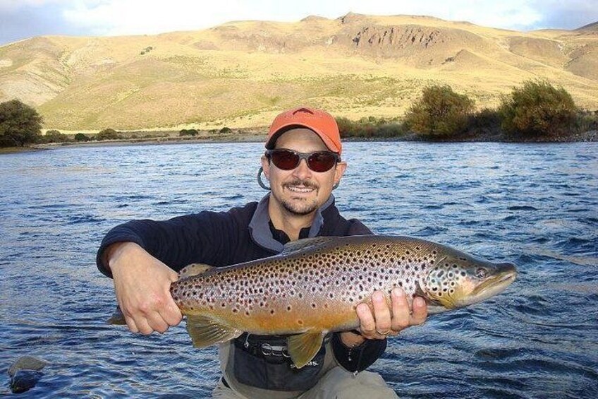 A person holding a large fish in a river with hills in the background. 1