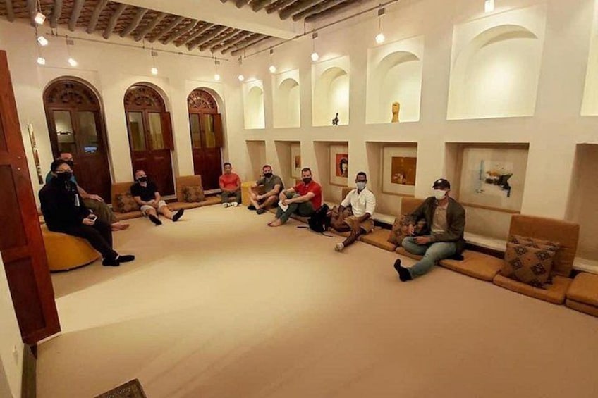 A group of people seated in a room with arched ceilings and a light-colored floor. 1