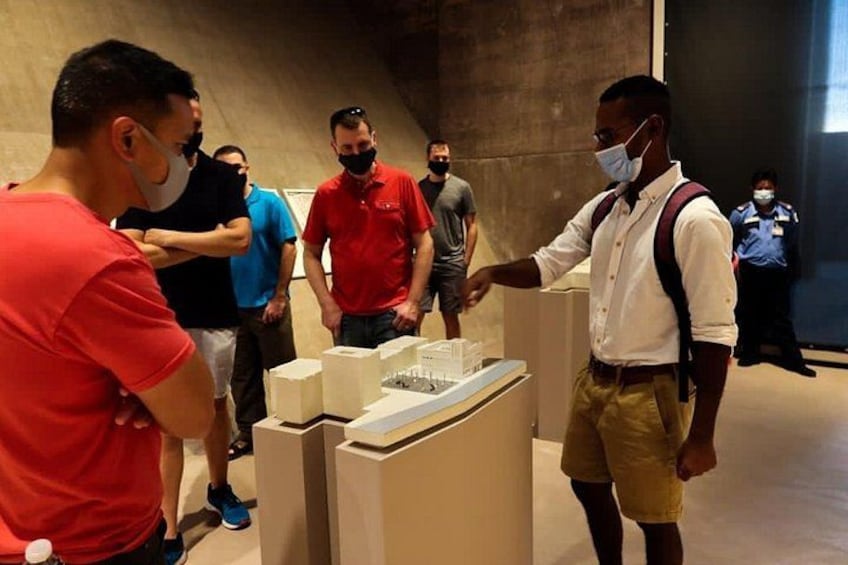 A group of people in a museum-like setting, examining a display with models and informational panels. 4