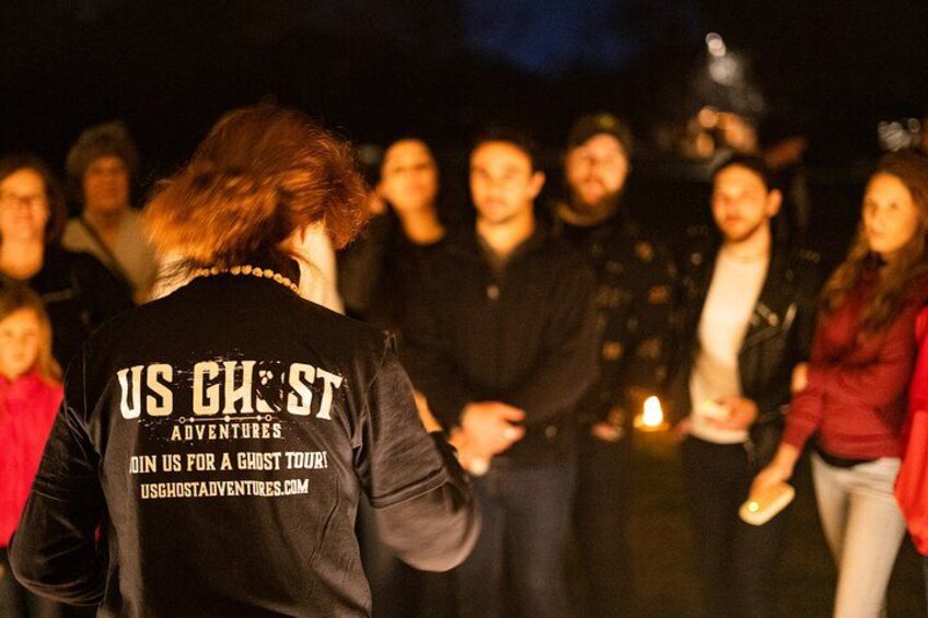 A group of people gathered around a person wearing a black jacket with text on the back. 2