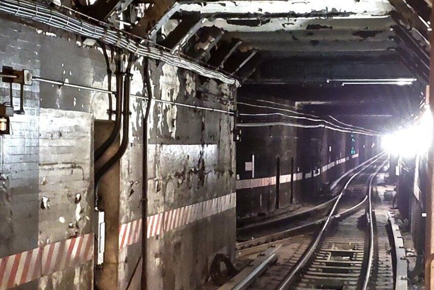 En jernbanetunnel med spor, overliggende ledninger og en kraftig lyskilde i enden. 2