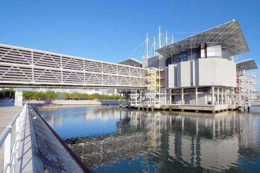 Een modern gebouw aan het water met een spiegelend wateroppervlak, een brug en een heldere lucht. 2