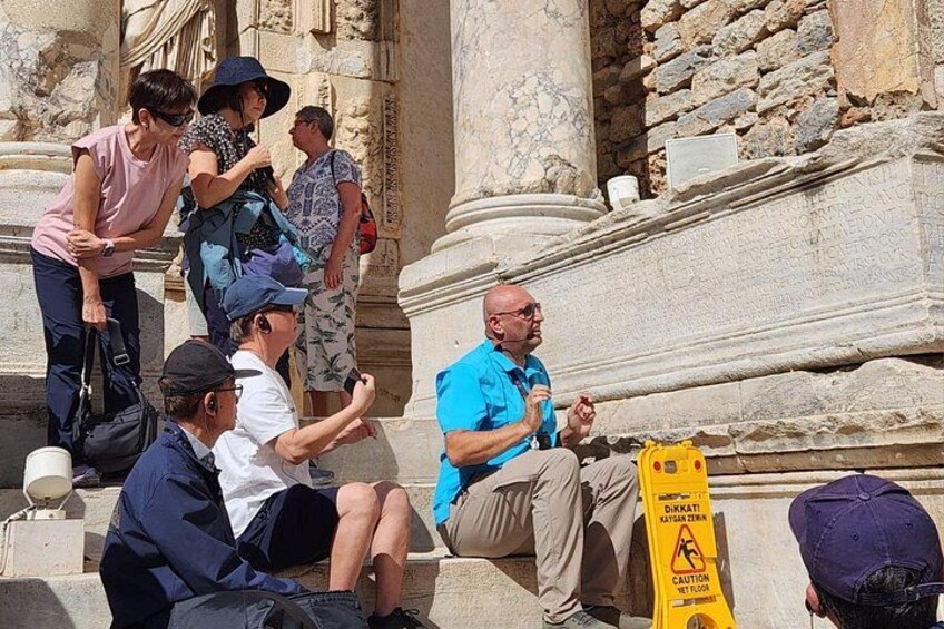 People sitting and standing near ancient ruins with columns and a caution sign. 5