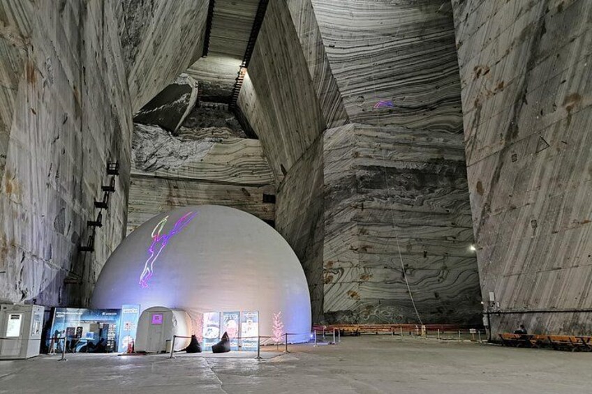 Una gran estructura blanca en forma de cúpula con superficie reflectante, rodeada de muros altos y con textura. 3