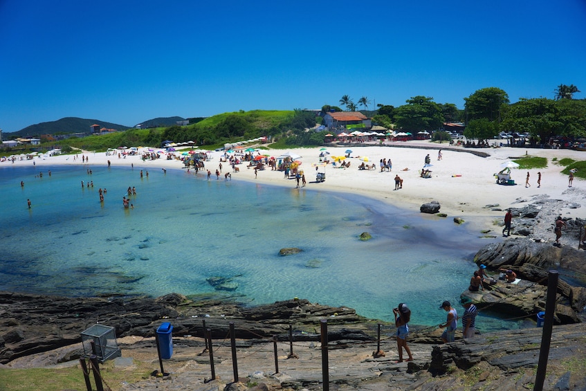 Une plage avec une eau claire, des gens qui se baignent et des parasols. 1