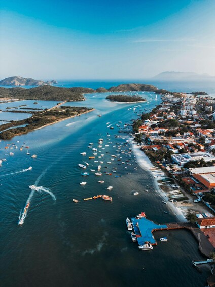 Vue aérienne d’une ville côtière avec un port de plaisance rempli de bateaux, entourée de collines et surplombée d’un ciel bleu clair. 2