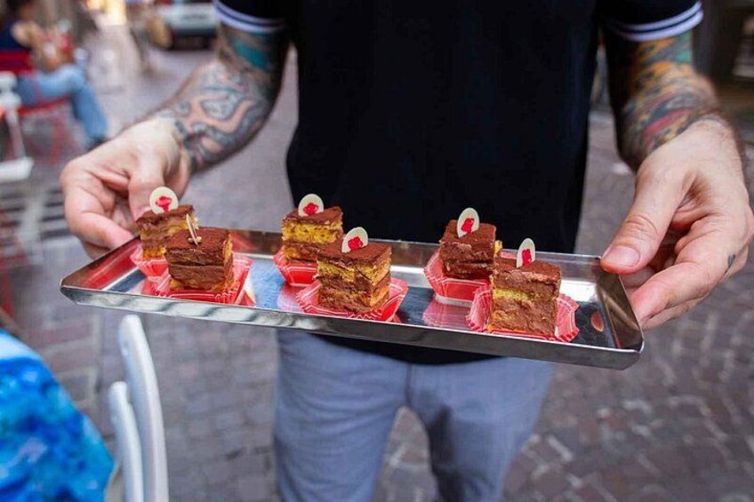 A person holding a tray with several square desserts, each topped with a small red decoration. 4