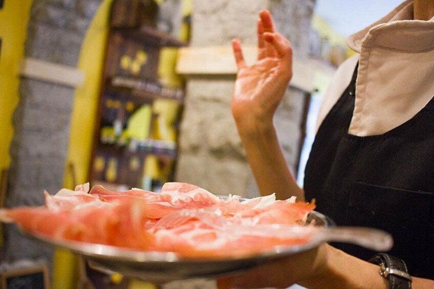 A person holding a plate with sliced meat, wearing a white shirt and black apron. 3