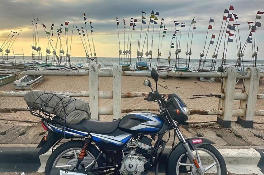 A blue motorcycle parked on a beach with sailboats in the background. 3